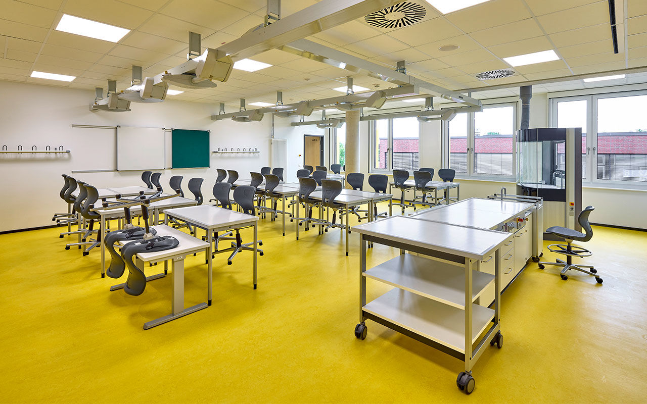 Flexibel nutzbarer Sonderraum im Neubau des Schulcampus Süd mit mobiler Ausstattung, höhenverstellbaren Arbeitstischen und farblich hervorgehobenem gelben Bodenbelag. Die gemeinsam von IGS und Realschule nutzbaren Fach- und Unterrichtsräume unterstützen das schulübergreifende Raumkonzept des Campus.